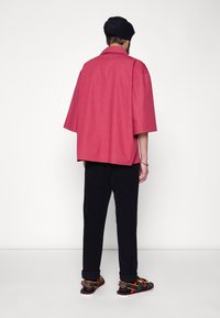 Losse korte mouwen chemise in koraal, van katoenmateriaal; gecombineerd met zwarte broek en sneakers met oranje accenten en een gestructureerde zool.