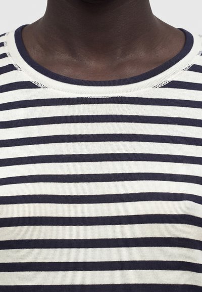 Κοντινό πλάνο ενός ατόμου που φοράει μπλούζα με οριζόντιες ριγέ navy μπλε και λευκές και στρογγυλή λαιμόκοψη.