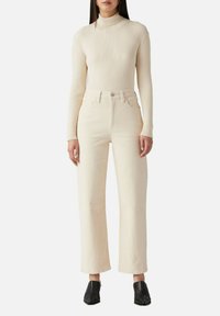 Pullover a colletto alto a coste crema abbinato a jeans di colore beige chiaro a vita alta e gamba larga. Stivaletti neri con tacco completano il look.