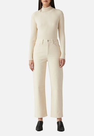 Pullover a colletto alto a coste crema abbinato a jeans di colore beige chiaro a vita alta e gamba larga. Stivaletti neri con tacco completano il look.