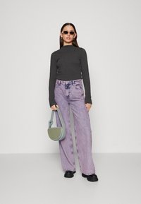 Grå ribbet langermet topp, lys lilla vide jeans og svarte klumpete sko. Holder en grønn skulderveske med avrundet design.