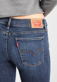 Dark blue denim jeans with a leather label displaying "Levi Strauss & Co." and yellow stitching on pockets, featuring a signature back pocket design.