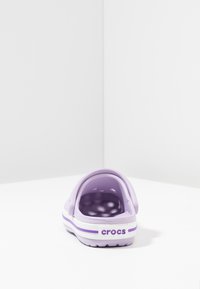 Lila Crocs med baksnodd, gjorda av lätt material, med ventilationshål, vita och lila ränder på sålen och logotyp.