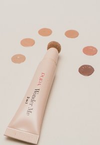 Pupa Wonder Me 3-in-1 Make-up-Tube, hellrosa, mit einer abgerundeten Applikatorspitze. Umgeben von farbigen Proben verschiedener Hauttöne in kreisförmigen Anordnungen.