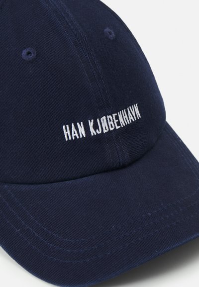 Sötétkék pamut sapka ívelt peremmel, elöl fehér hímzett "HAN KJOBEHAVN" felirattal és texturált szövet részletekkel.