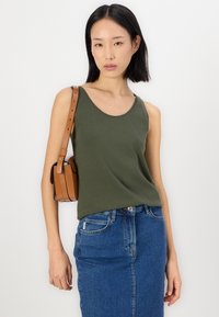 Olive green tank top with a round neckline, paired with a denim skirt. A small brown crossbody bag with a strap is worn over one shoulder.