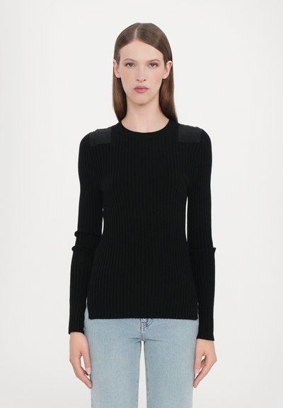 Suéter negro acanalado con un diseño ajustado, mangas largas y sutiles acentos en los hombros. Combinado con unos jeans de mezclilla azul claro.