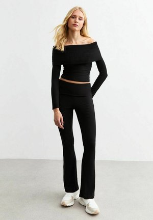 Black ribbed knit crop top with off-the-shoulder neckline paired with matching flared pants. Worn with white chunky sneakers.
