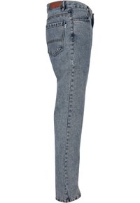 Jean en denim bleu délavé présenté de profil avec une poche arrière, des passants de ceinture et une pièce en cuir marron sur la ceinture.