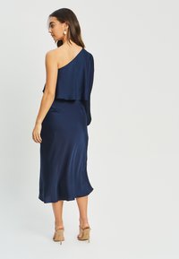 Navy satin dress with one shoulder design, flowing fabric, and a knee-length hem. Features a layered top and minimal hardware accents.