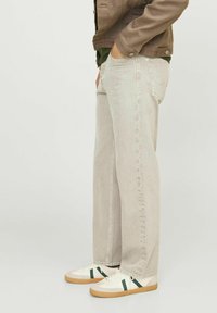Vaqueros de mezclilla gris claro con un corte recto, que cuentan con bolsillos traseros y un aspecto casual, combinados con zapatillas blancas y detalles en verde.