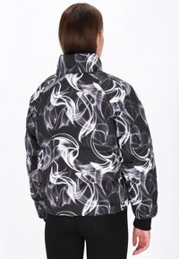 Pufferjakke med et sort og hvidt svungent mønster, der har en høj krave, elastiske manchetter og en polstret tekstur.