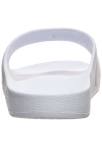 Tong en caoutchouc blanc avec une surface texturée, dos ouvert et larges brides. Design minimaliste, adapté à une tenue décontractée.