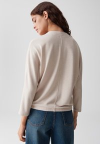 Beige gerippter Oberteil mit Dreiviertelärmel, rundem Ausschnitt und geradem Saum, kombiniert mit blauen hochtaillierten Jeans.