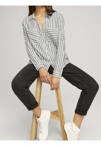 Gestreepend shirt in lichtgrijs en wit, met een kraag, twee borstzakken en lange mouwen, gecombineerd met opgerolde zwarte jeans en witte sneakers.