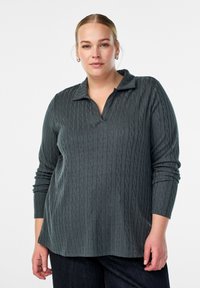 Tamno sivi pleteni pulover s teksturiranim uzorkom pletenice, s okovratnikom i dugim rukavima, u kombinaciji s tamnim trapericama.