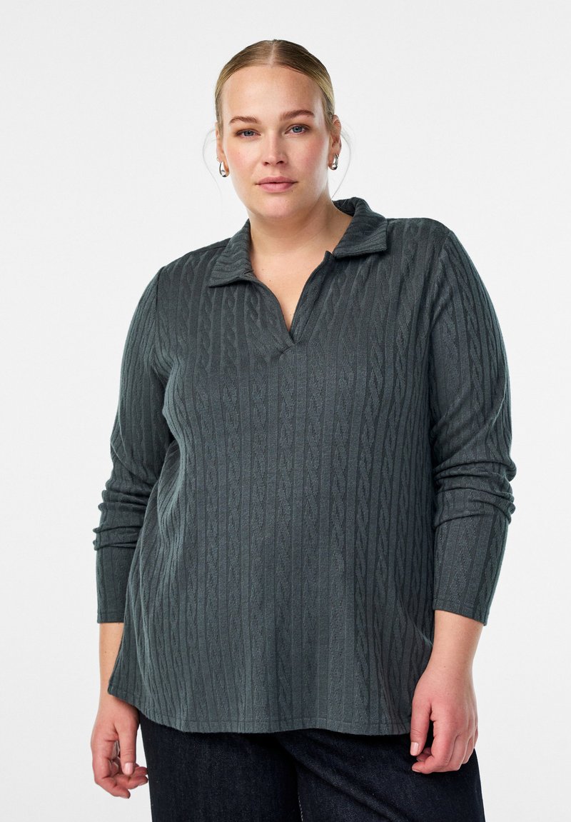 Tamno sivi pleteni pulover s teksturiranim uzorkom pletenice, s okovratnikom i dugim rukavima, u kombinaciji s tamnim trapericama.