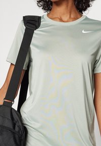 Camiseta atlética verde claro hecha de tejido suave, con escote redondo y mangas cortas, con un logo blanco de Nike en el pecho.