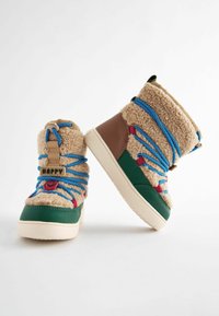 Bottes beige et verte floues avec des lacets bleus et rouges, des accents beiges et un détail de logo rond. Elles possèdent une tige texturée et une semelle robuste.