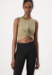 Olive green cropped tank top with a twisted front detail, paired with black high-waisted pants. Smooth fabric with a fitted silhouette.