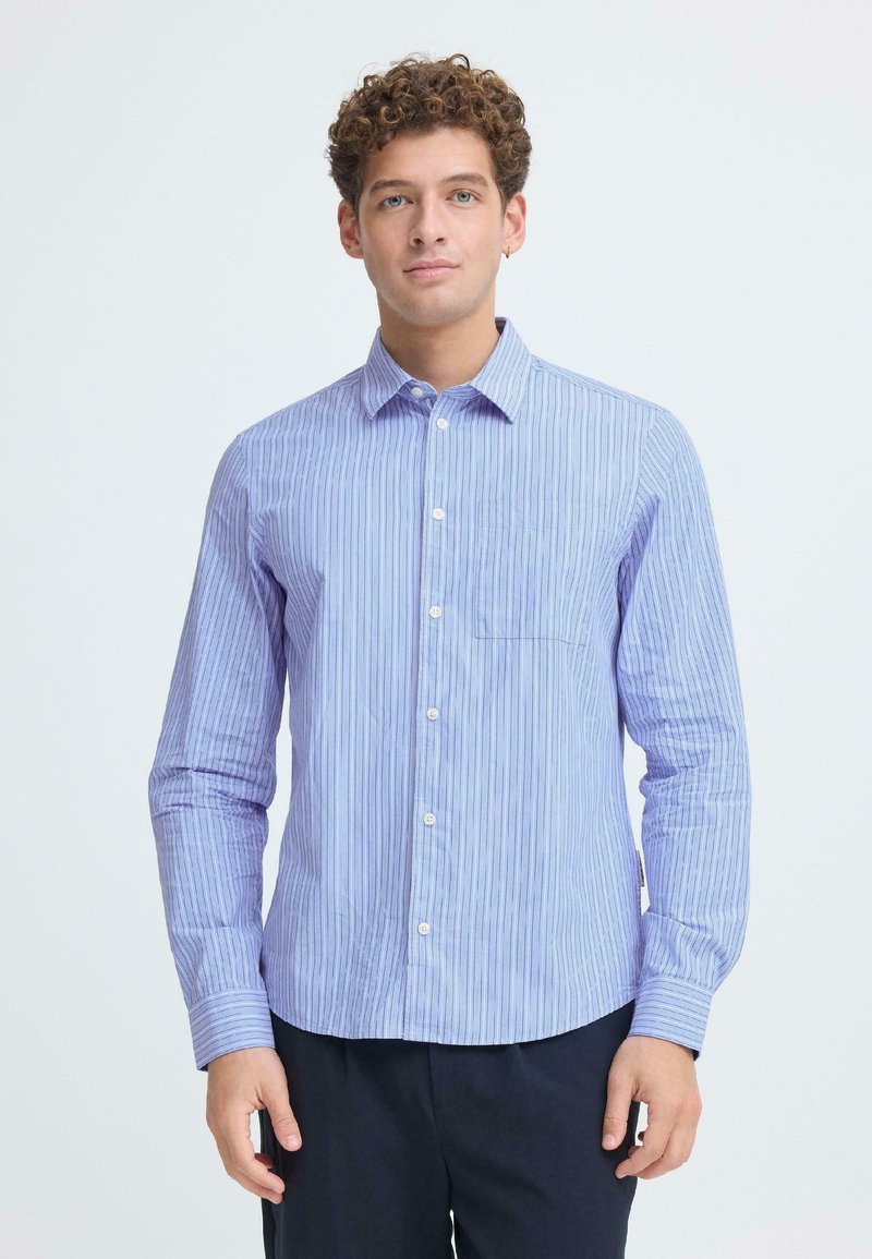 Ανοιχτό μπλε ριγέ πουκάμισο με κουμπιά, μακρυά μανίκια, γιακά και τσέπη στο μπροστινό μέρος. Το ύφασμα έχει ομαλή υφή και διακριτική γυαλάδα.