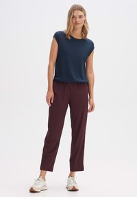 Top corto a maniche corte di un blu navy testurizzato abbinato a pantaloni elasticizzati bordeaux con vita alta e scarpe da ginnastica bianche con suola marrone; vestibilità comoda e semplicità.