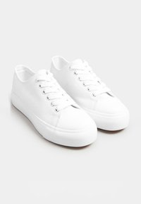 Vita canvas-sneakers med rund tå och platt gummisula. Sex öglor för snörning med platta snören. Texturerat tyg och mjuk inredning.