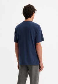 Námořnická modrá bavlněná tričko s klasickým kulatým výstřihem, krátkými rukávy a volným střihem, zobrazené zezadu s hladkou strukturou.