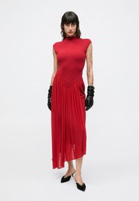 Czerwona sukienka z dopasowanym gorsetem i zwiewnym, przejrzystym dołem. Charakteryzuje się wysokim dekoltem i krótkimi, bufkowatymi rękawkami. Uzupełniona czarnymi rękawiczkami.