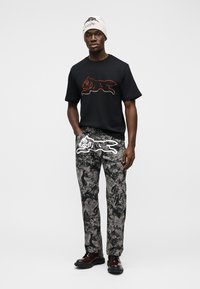 Μαύρο βαμβακερό t-shirt με σχέδιο ζώου από κόκκινους στρας, συνδυασμένο με γκρι παντελόνι με μοτίβο άσπρου ζώου. Το σύνολο ολοκληρώνουν καφέ παπούτσια.