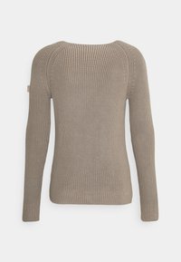 Pull en tricot côtelé beige avec manches longues, présentant un col rond et une texture subtile. Inclut une petite étiquette avec logo sur la manche.