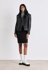 Crna kožna motorista jakna preko prugaste gola majice, uparen s crnom olovka suknjom i bijelim cipelama s crnim potplatima i detaljima.