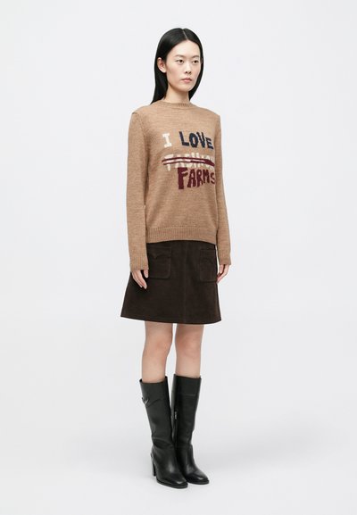 Rjavo pleten pulover z napisom “I LOVE FARMS”, kombiniran s temno rjavo semiš krilo z žepi in črnimi usnjenimi škornji do kolen.