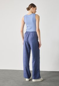 Lys blå ribbestrikket tank topp kombinert med myke, mørkeblå, vide bukser med et teksturert mønster. Modellen ses fra ryggen.