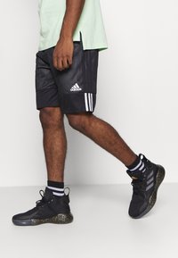 Pantalones cortos deportivos de malla negros con tres rayas blancas y zapatillas altas negras con una suela dorada moteada y calcetines a rayas.