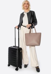 Valigia nera rigida con design a righe, ruote rotolanti e manico retrattile, abbinata a una borsa a tracolla in tessuto marrone chiaro.