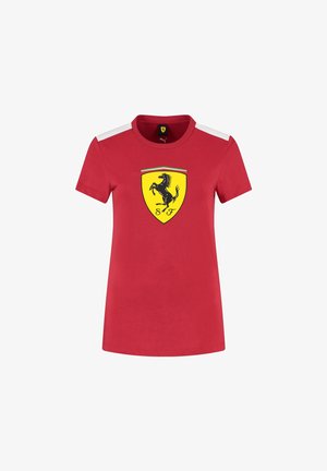 Czerwona koszulka z krótkim rękawem wykonana z bawełny. Posiada czarne logo Ferrari na żółtej tarczy oraz białe akcenty na ramionach.