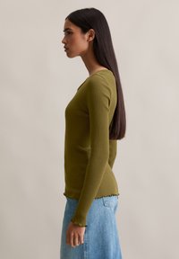 Haut long à manches ribbed et mince en vert olive, avec un col rond et un ourlet en feston. Associé à une jupe en denim bleu clair.