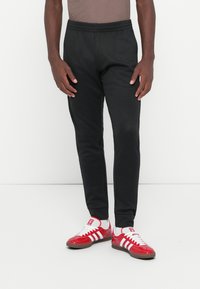 Pantaloni de trening negri cu talie elastică și șnur, cu croi ajustat și buzunare laterale, asortați cu pantofi sport roșii cu dungi albe.
