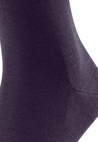 Primo piano di un calzino viola scuro, che mette in evidenza una texture liscia, a coste e un design aderente.