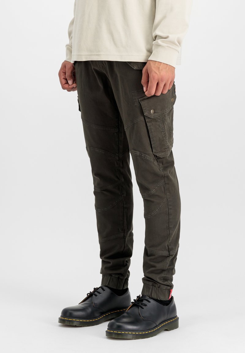 Pantaloni cargo din material verde închis, cu buzunare laterale, design conic și mansete elastice. Asortați cu pantofi negri cu șireturi și o cămașă ușoară.