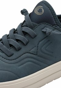 Blauer Sneaker mit einer glatten Oberseite, strukturierten grauen Schnürsenkeln und dezentem Wellenmuster. Verfügt über eine weiße Gummisohle und ein Markenlogo auf der Zunge.