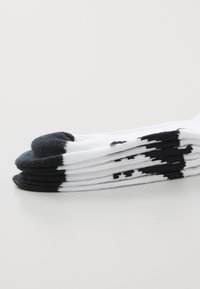 Vita strumpor med svart tå och häl, med en svart mönstrad design längs toppen, prydligt staplade på en vit yta.