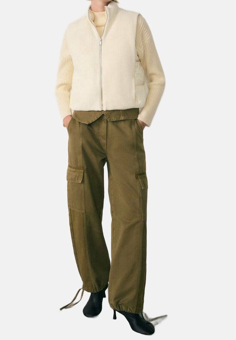Personne portant un gilet beige zippé, un pull en maille crème, un pantalon cargo olive avec cordons et des bottines noires à talons, mains dans les poches.