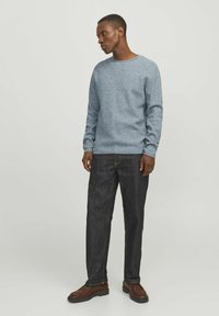 Helles blaues strukturierte Sweatshirt mit Rundhalsausschnitt, kombiniert mit dunkelblauen Jeans und braunen Schuhen. Das Outfit hat eine lässige Passform.