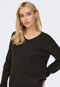 Brun ribbestrikket genser med V-hals, lange ermer og en avslappet passform, med teksturert stoff og synlige sømdetaljer.