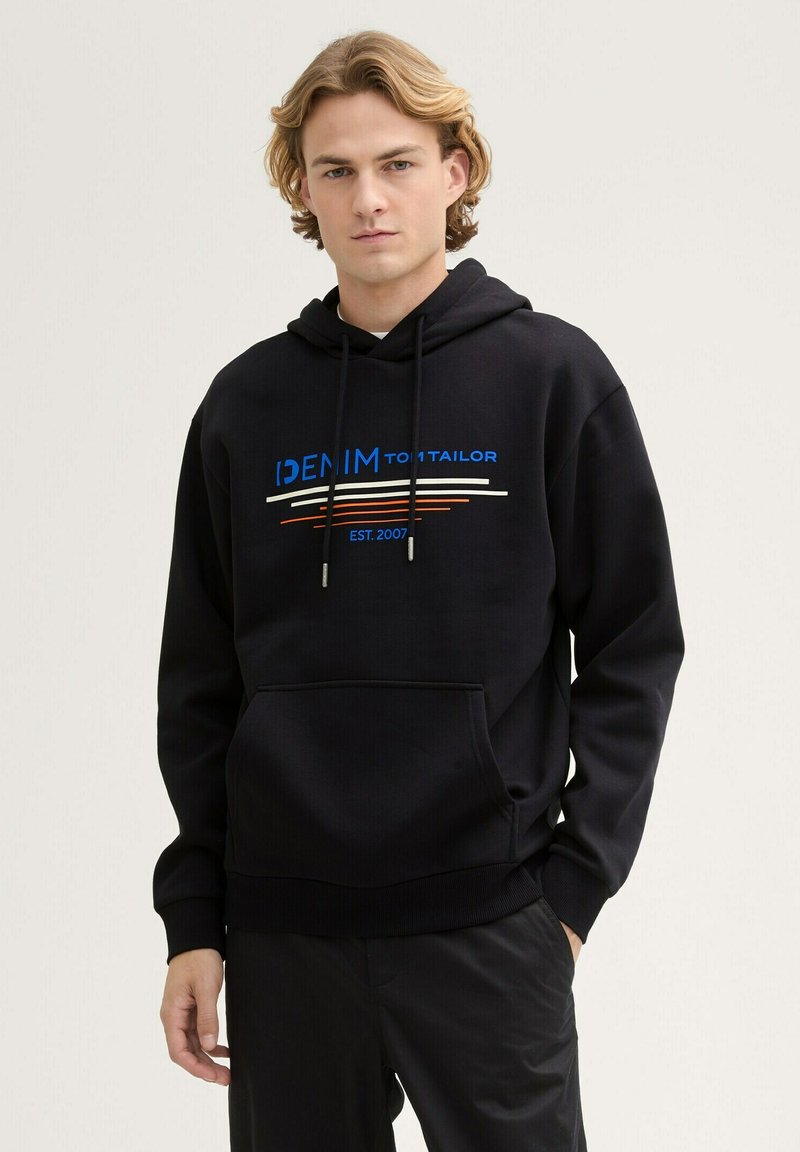 Sudadera negra con capucha y un bolsillo frontal, que presenta un estampado colorido: "DENIM TOM TAILOR" y líneas horizontales en azul, rojo y crema.