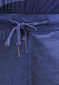 Mörkblå joggerbyxor med dragsko i midjan, med en texturerad tyg och silvriga ändar på dragskorna.