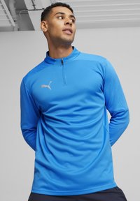 Blaues sportliches Langarmshirt mit Viertelreißverschluss-Kragen, strukturiertem Stoff und silbernem Puma-Logo auf der linken Brust.