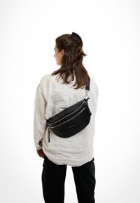 Black leather fanny pack with two zippered compartments, adjustable strap, smooth texture, and minimal branding on the front.